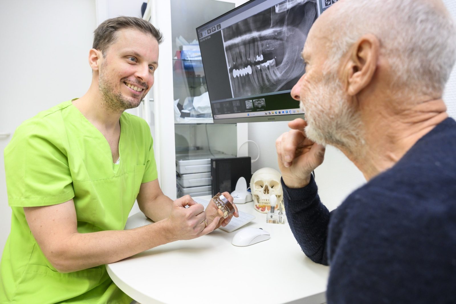 Dr. Ansgar Hergt erklärt einem Patienten die 3D-Aufnahme und ein Implantatmodell - Beratung in der Praxis Oralchirurgie Templin